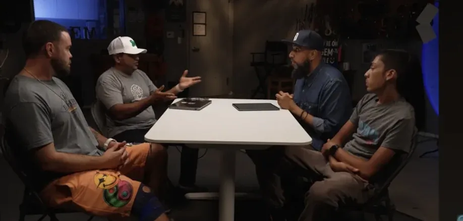Four people in conversation around a table on the KGEM studio set