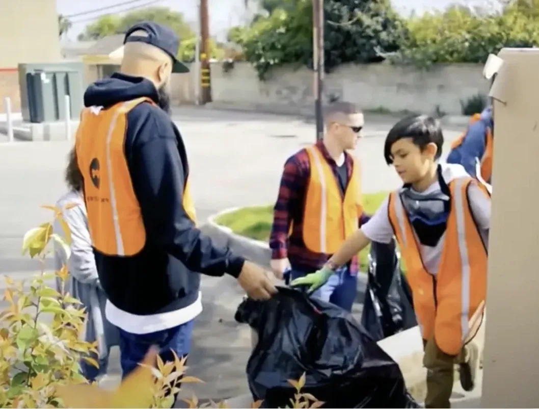 Volunteers in orange safety vests bagging trash along a Monrovia street