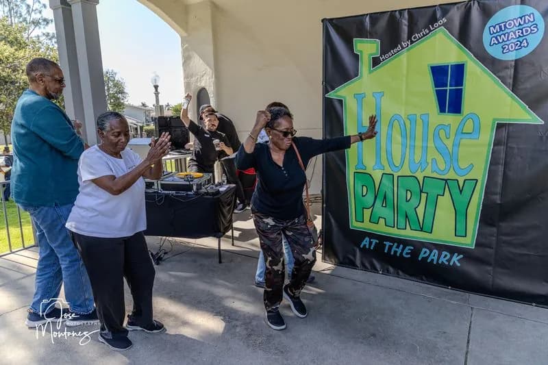 Neighbors dancing in front of the House Party at the Park banner at the bandshell